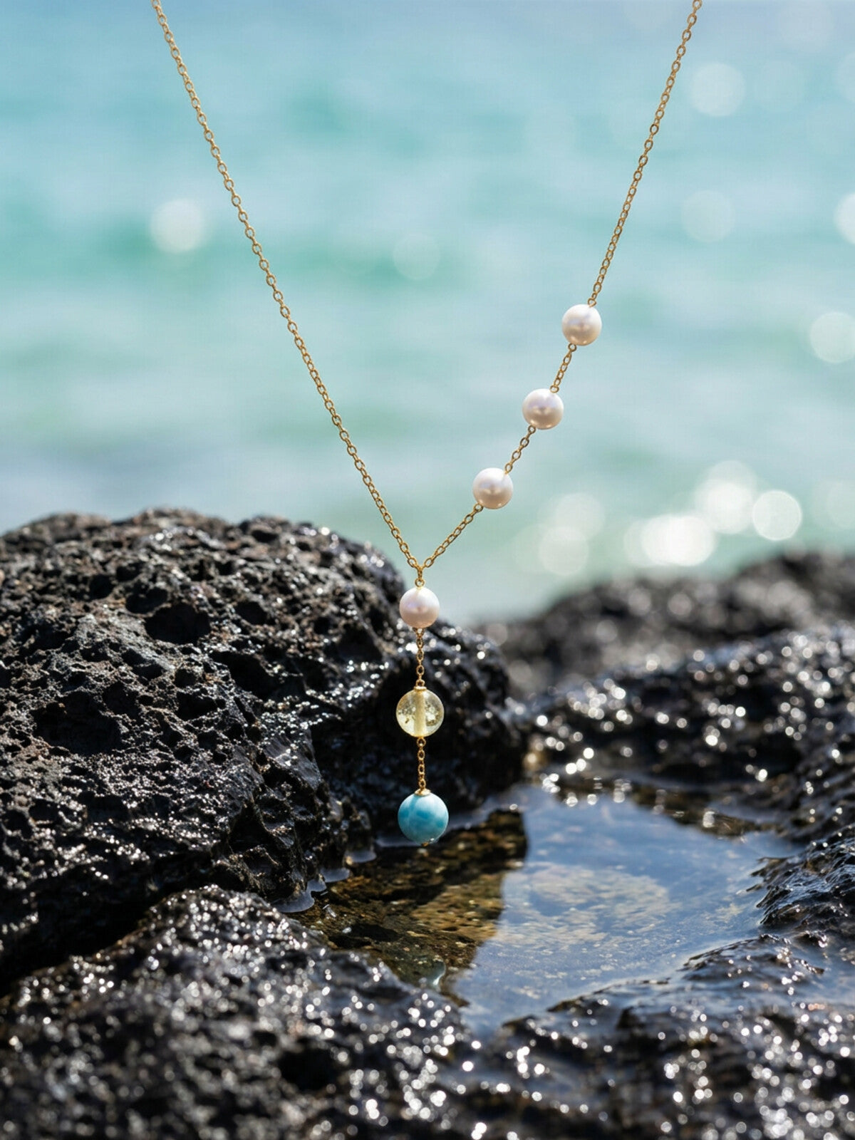 Larimar, amber and pearl pendant necklace, photographed on the beach
