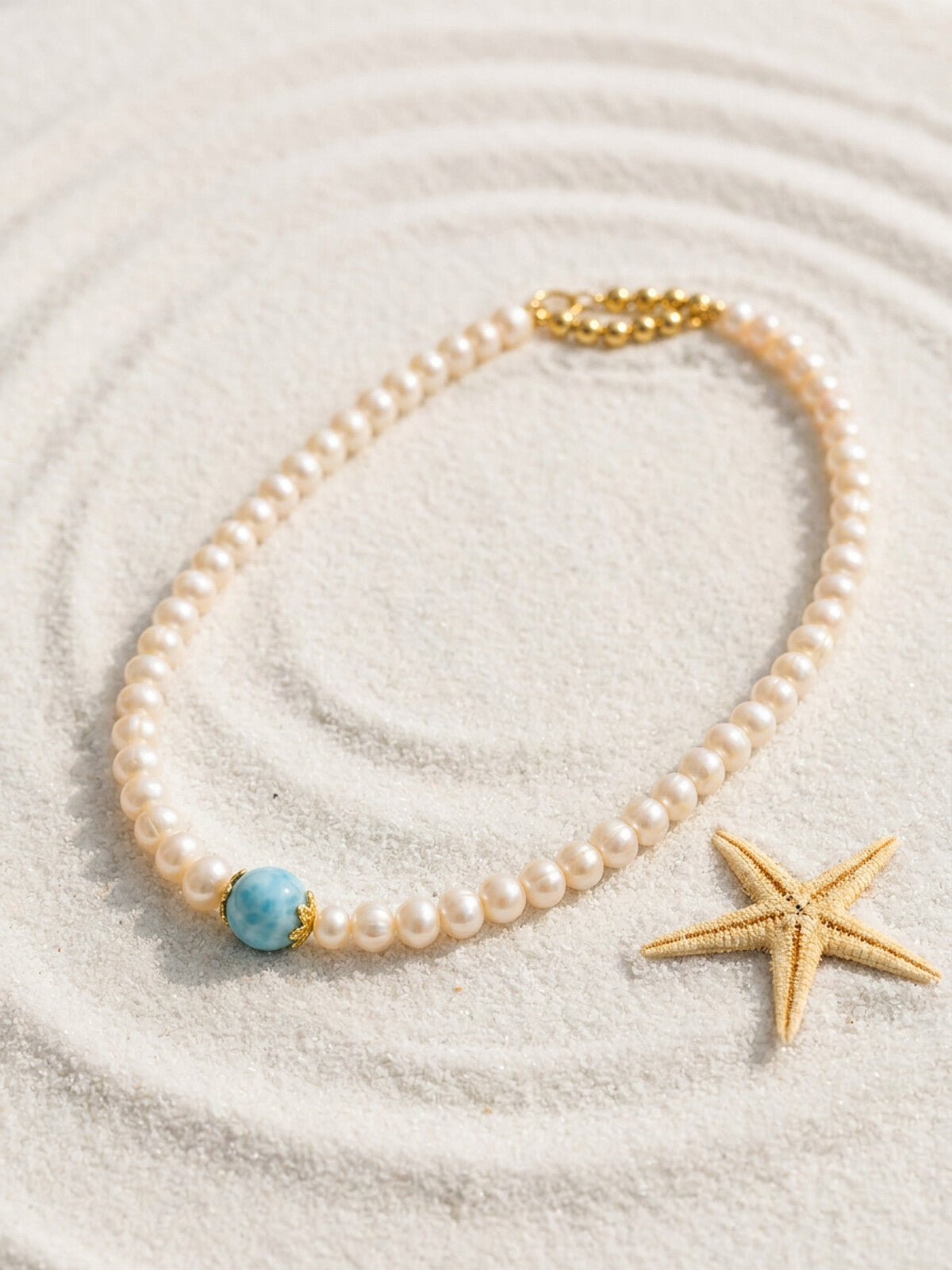 Pearl necklace with larimar bead, photographed on the beach